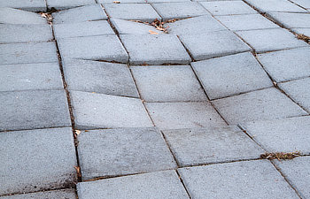 sidewalk of concrete tiles that are starting to sink and have created a depression