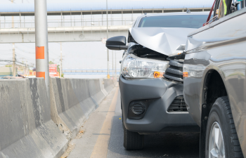 Two vehicles in a rear-end collision on a highway, with the front of one car crumpled against the back of another, next to a concrete barrier.