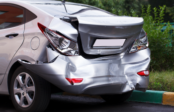 A silver car with significant rear-end damage parked near a curb.