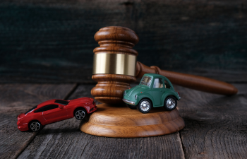 A judge's gavel with two toy cars, one red and one green, positioned on a wooden surface.